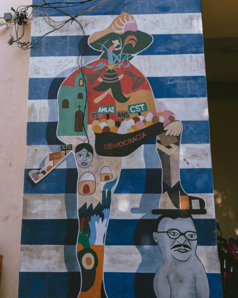 Nicaragua Travel Guide: Land of Lakes and Volcanoes 8 A mural on a blue and white striped wall, featuring a large figure with its foot squashing a political opponent, in León, Nicaragua.