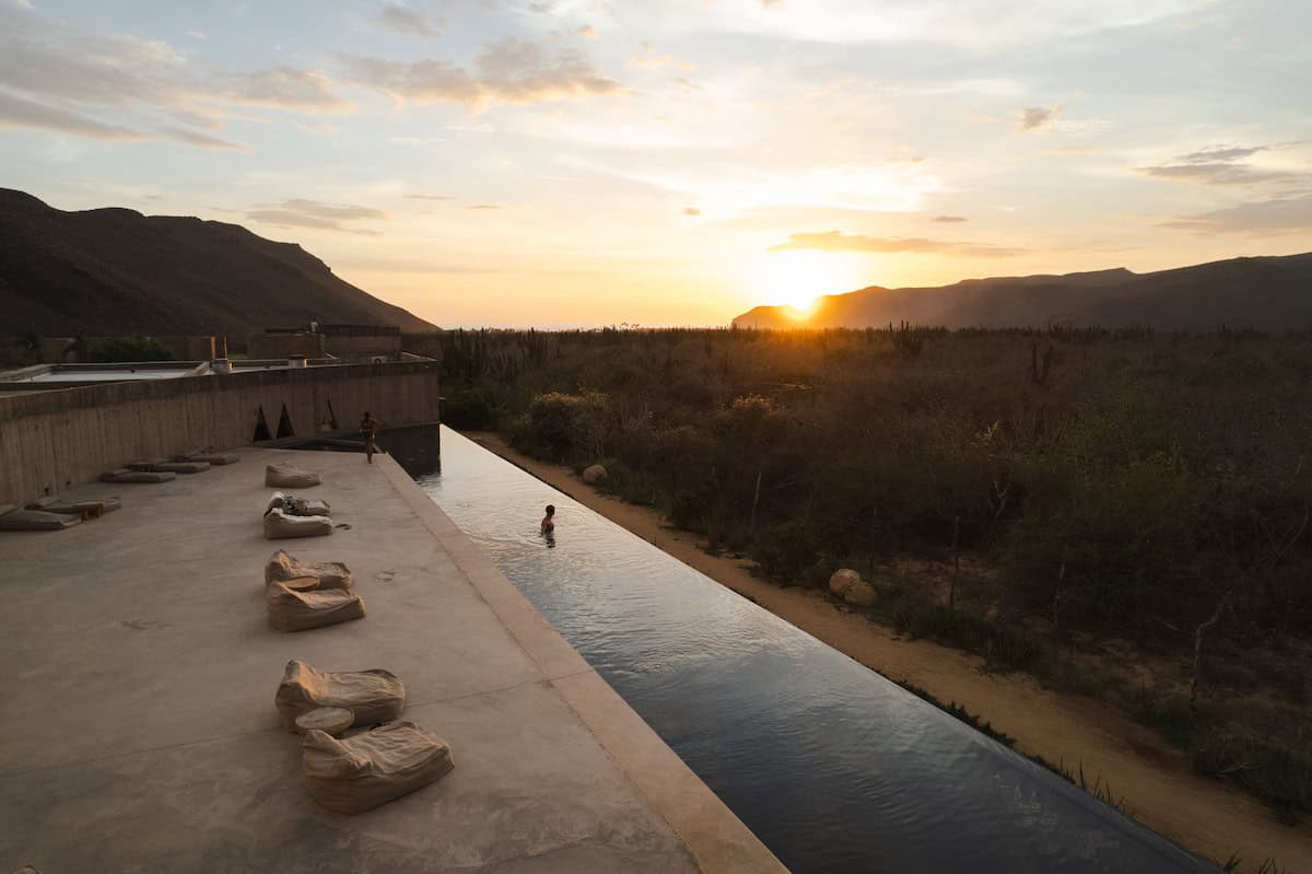 Where to Stay in Todos Santos, Mexico: Hotel & Area Guide 24 A tranquil infinity pool stretches into the desert horizon as the sun sets behind the mountains near Todos Santos, creating a serene and minimalist oasis.