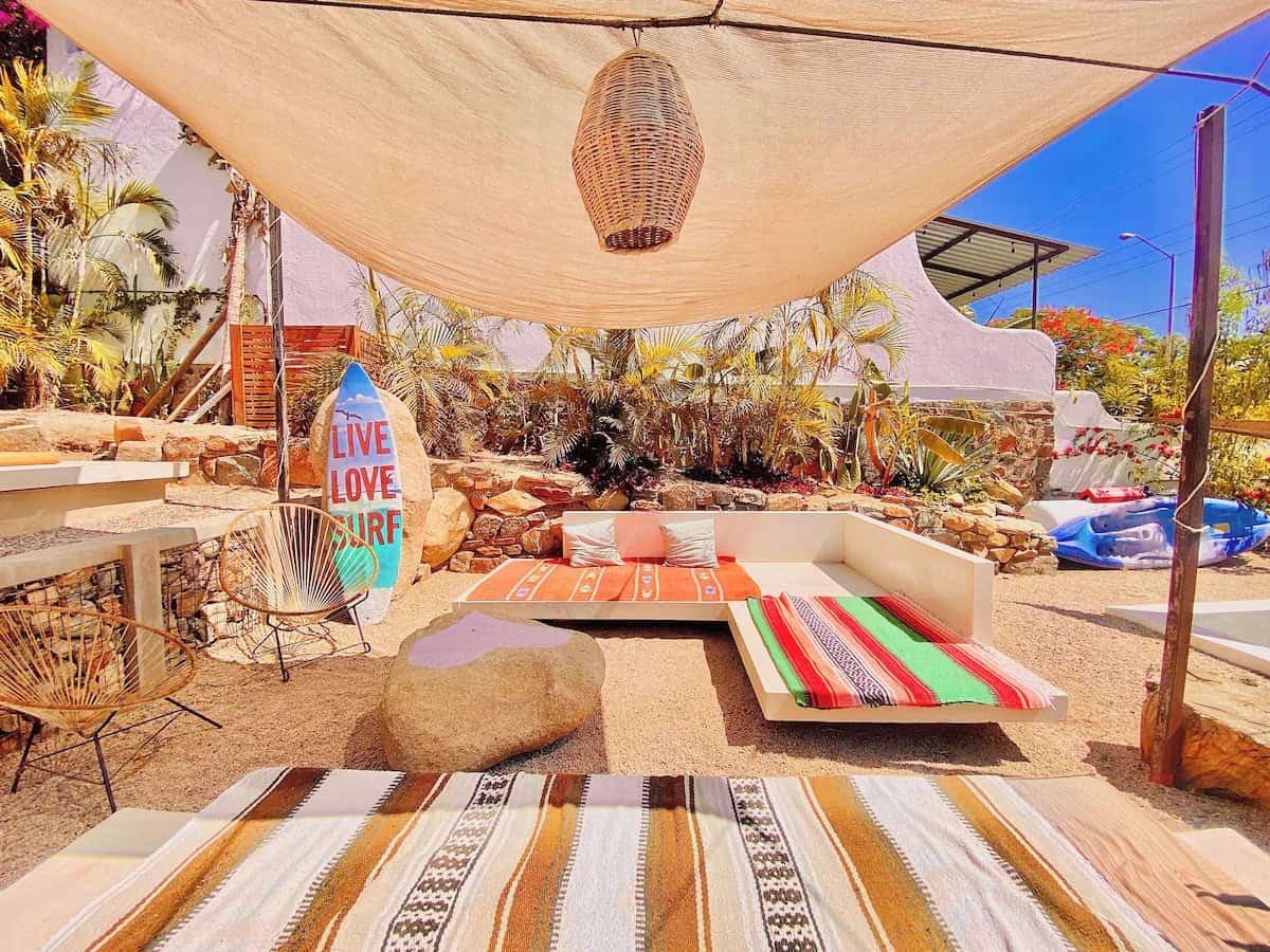12 Best Things to Do in Todos Santos Mexico Travel Guide 49 A vibrant and cozy surf hostel patio in Baja, decorated with colorful Mexican blankets, lounge seating, woven chairs, and a surfboard sign that reads “Live Love Surf.”