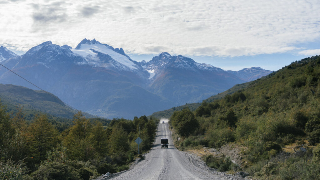 The Carretera Austral, Chile: Everything You Need to Know 55 A rugged gravel road cuts through dense greenery and leads toward the dramatic, snow-capped peaks of the Andes near Cochrane, Chile, with a black camper van driving into the distance