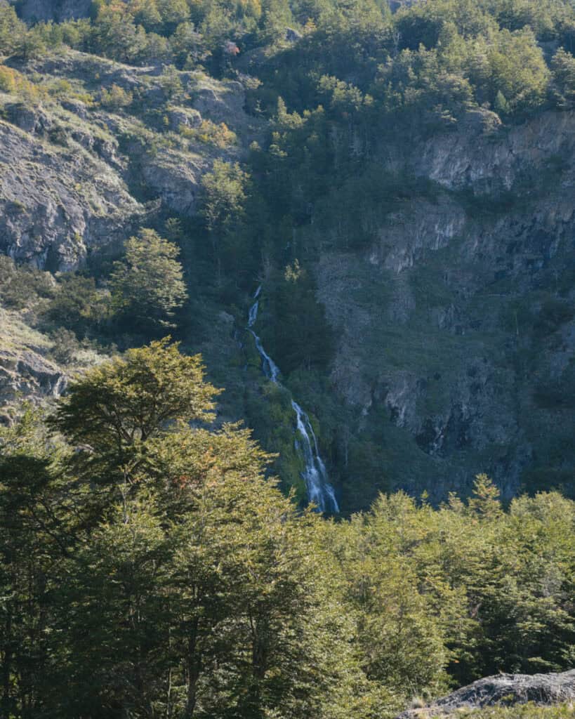 Tamango Sector Guide: Parque Nacional Patagonia, Chile 2 Distant waterfall descending through a forested mountain ravine, surrounded by green trees and rugged cliffs