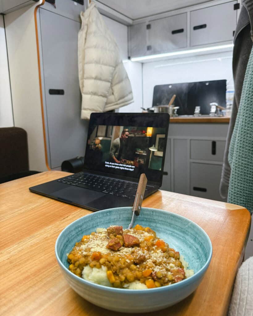 Valle Chacabuco Sector Guide: Parque Nacional Patagonia, Chile 49 A cozy camper van interior with a bowl of lentils and mashed potatoes on a table in front of a laptop playing a movie, steam rising from the cooking area in the background