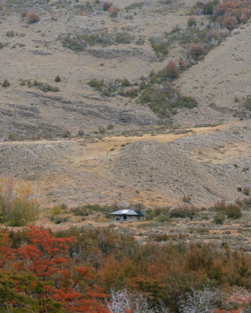 Valle Chacabuco Sector Guide: Parque Nacional Patagonia, Chile 28 A small cabin stands isolated in a wide Patagonian valley, surrounded by dry shrubs and distant red-tipped trees under a cloudy sky