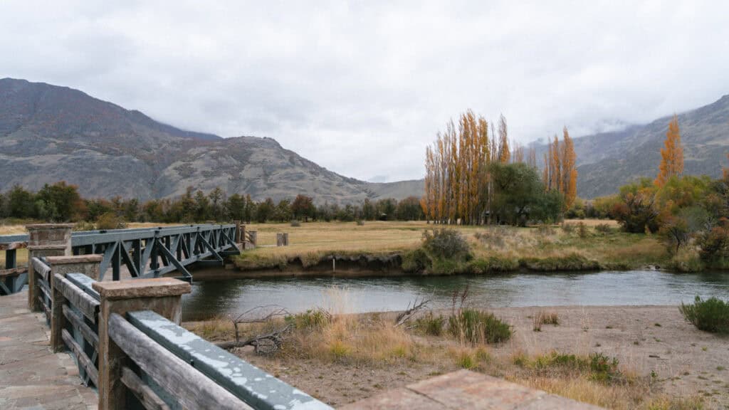 Valle Chacabuco Sector Guide: Parque Nacional Patagonia, Chile 26 A rustic bridge spans a calm river with tall autumn trees and mountain slopes in the background, captured near Casa de Piedra campground in Patagonia