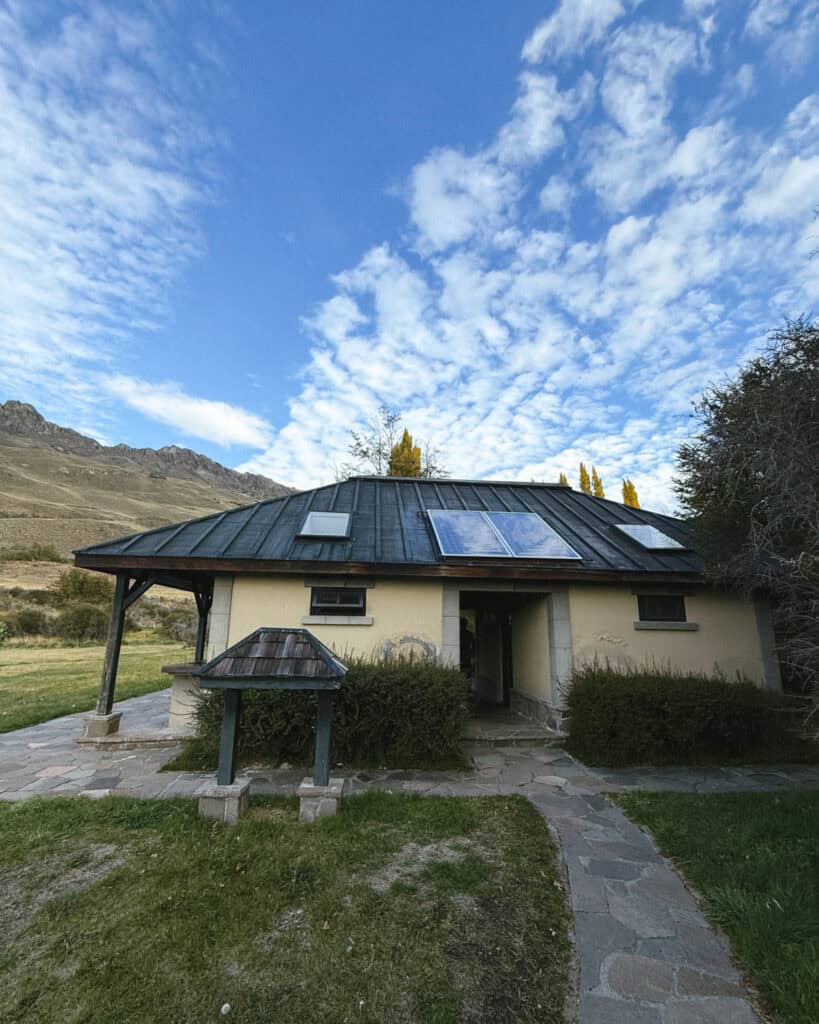 Valle Chacabuco Sector Guide: Parque Nacional Patagonia, Chile 21 A low stone building with a dark green metal roof and solar panels, set in a grassy clearing with a backdrop of rocky hills and partly cloudy blue sky