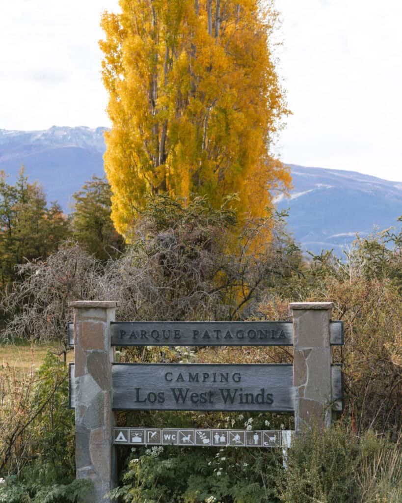 Valle Chacabuco Sector Guide: Parque Nacional Patagonia, Chile 22 A close-up of the stone and wood sign reading "Camping Los West Winds" with a tall yellow tree behind it and mountains in the distance