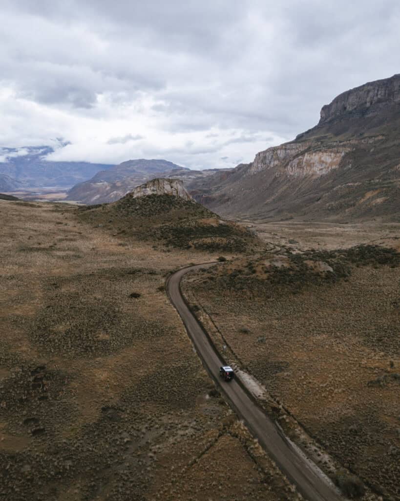 Valle Chacabuco Sector Guide: Parque Nacional Patagonia, Chile 2 Drone shot of a black camper van travels a winding dirt road through the arid highlands of Patagonia, with dramatic rocky hills and cloudy skies in the distance