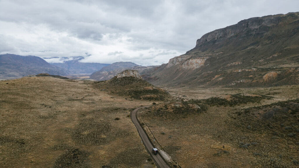 The Carretera Austral, Chile: Everything You Need to Know 56 A wide aerial view of a camper driving through a winding dirt road in a vast, brown Patagonian valley bordered by dramatic cliffs