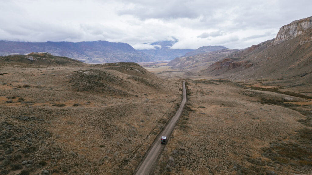 Valle Chacabuco Sector Guide: Parque Nacional Patagonia, Chile 16 A long shot of a camper van moving through a remote, desolate highland landscape with cloudy skies and layered mountains in the background