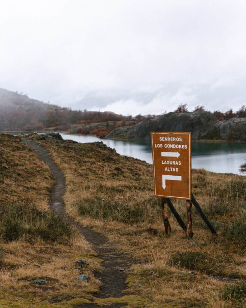 Valle Chacabuco Sector Guide: Parque Nacional Patagonia, Chile 30 Wooden directional sign at a lake junction points toward Senderos Los Cóndores and Lagunas Altas, set beside a winding dirt trail and turquoise water