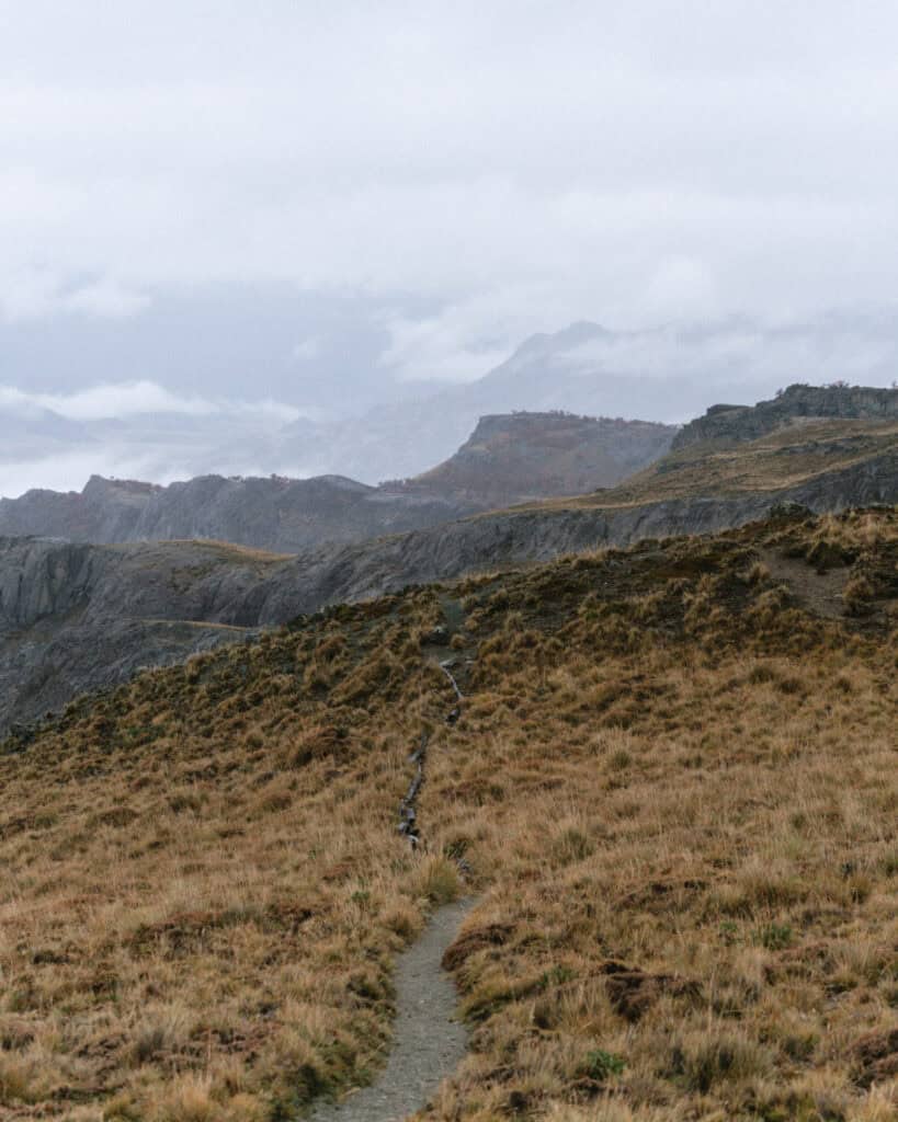 Valle Chacabuco Sector Guide: Parque Nacional Patagonia, Chile 41 A narrow dirt path winds uphill through dry grasslands toward distant ridges and misty mountains in Parque Nacional Patagonia