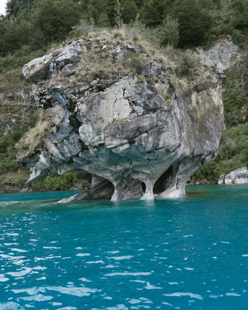 How to Visit the Marble Caves in Chile: Worth the Journey? 17 A single massive marble rock formation stands rooted in the blue waters of General Carrera Lake at Capillas de Mármol in Puerto Río Tranquilo, Chile, surrounded by lush green forest