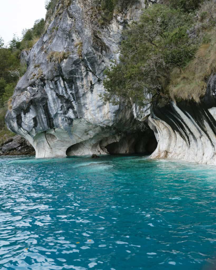 How to Visit the Marble Caves in Chile: Worth the Journey? 7 A wide view of the marble caves at Capillas de Mármol in Puerto Río Tranquilo, Chile, showing cave entrances surrounded by vibrant blue water and cliffside vegetation