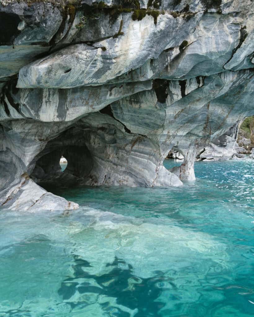 How to Visit the Marble Caves in Chile: Worth the Journey? 33 Arch-like openings and window-shaped rock features in the marble caves at Capillas de Mármol reflect beautifully on the still teal water in Puerto Río Tranquilo, Chile