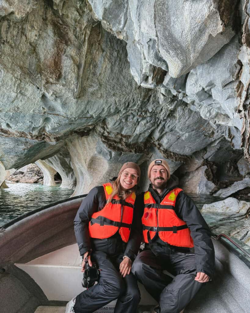 How to Visit the Marble Caves in Chile: Worth the Journey? 20 Sally and Brayden sit together in a boat inside the Capillas de Mármol caves in Puerto Río Tranquilo, Chile, both wearing orange life jackets and winter gear, framed by textured marble arches