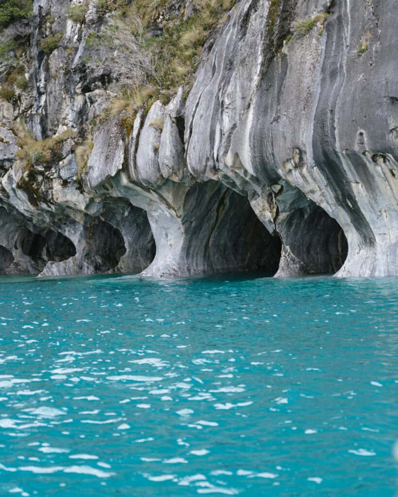 How to Visit the Marble Caves in Chile: Worth the Journey? 16 The dramatic striated marble cliffs of the Capillas de Mármol in Puerto Río Tranquilo form multiple cave openings above the blue-green water