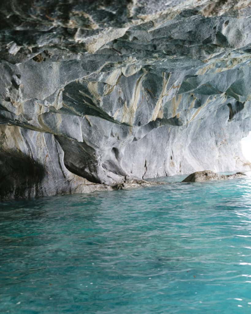 How to Visit the Marble Caves in Chile: Worth the Journey? 6 Inside one of the Capillas de Mármol caves in Puerto Río Tranquilo, light glows off teal water and illuminates the jagged, textured marble ceiling
