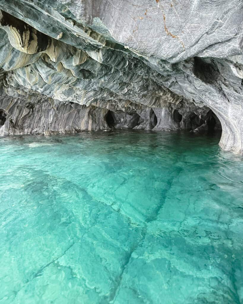 How to Visit the Marble Caves in Chile: Worth the Journey? 22 A wide view of a marble cave in Puerto Río Tranquilo showcases the glowing turquoise water beneath a sculpted ceiling of swirled grey and cream rock
