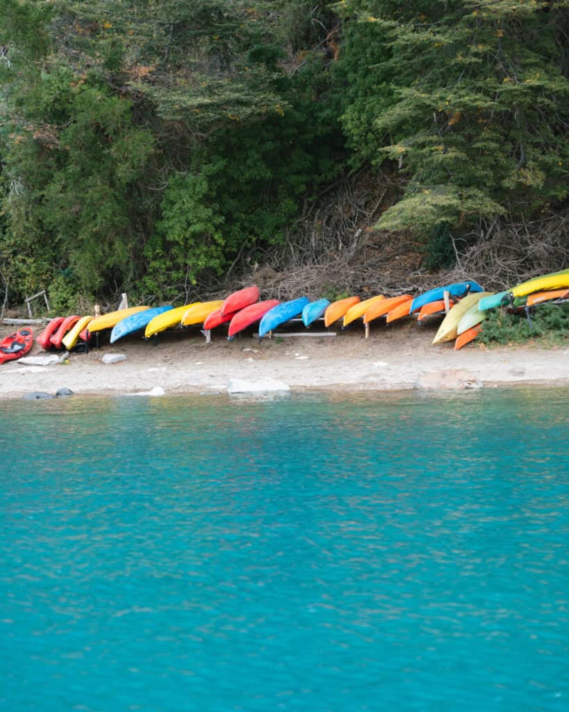 How to Visit the Marble Caves in Chile: Worth the Journey? 24 A shoreline in Puerto Río Tranquilo, Chile, lined with colorful kayaks in red, yellow, orange, blue, and green, arranged in a neat row against a backdrop of dense trees