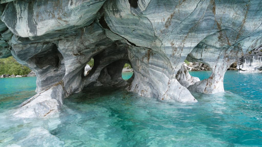 How to Visit the Marble Caves in Chile: Worth the Journey? 29 Intricate marble arches and tunnels surrounded by turquoise water at the Marble Caves in Puerto Río Tranquilo, with glimpses of greenery in the distance