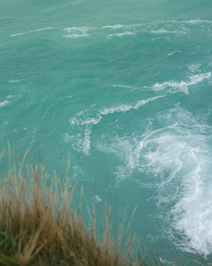 Puerto Rio Tranquilo, Chile Travel Guide: Marble & Ice 36 A close-up of teal river water swirling near the edge of a rocky bank with grassy foreground, capturing the energy of the Río Baker and Río Neff confluence