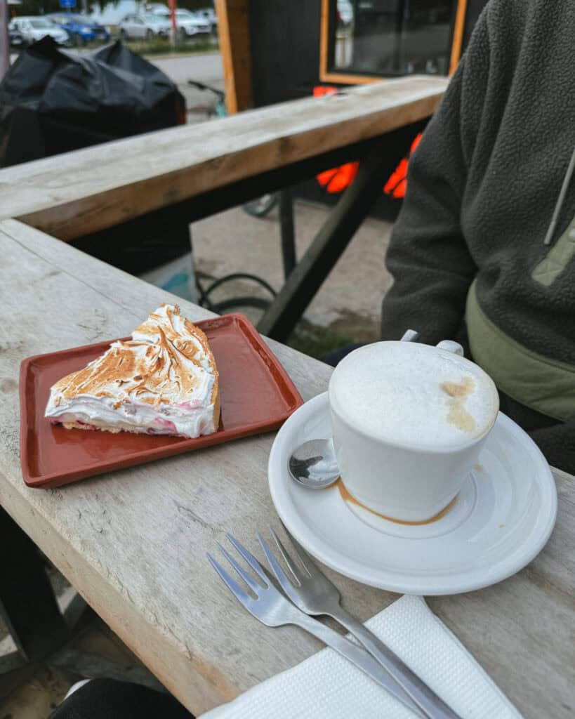 Puerto Rio Tranquilo, Chile Travel Guide: Marble & Ice 40 A slice of meringue-topped pie sits on a red plate beside a frothy cappuccino on a rustic outdoor table, with forks and napkins neatly arranged nearby