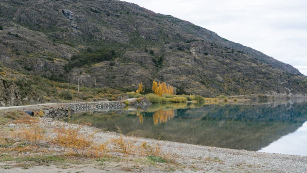 Puerto Rio Tranquilo, Chile Travel Guide: Marble & Ice 41 A quiet gravel road winds along the edge of a lake, where golden autumn trees reflect vividly in the still water under the looming hills