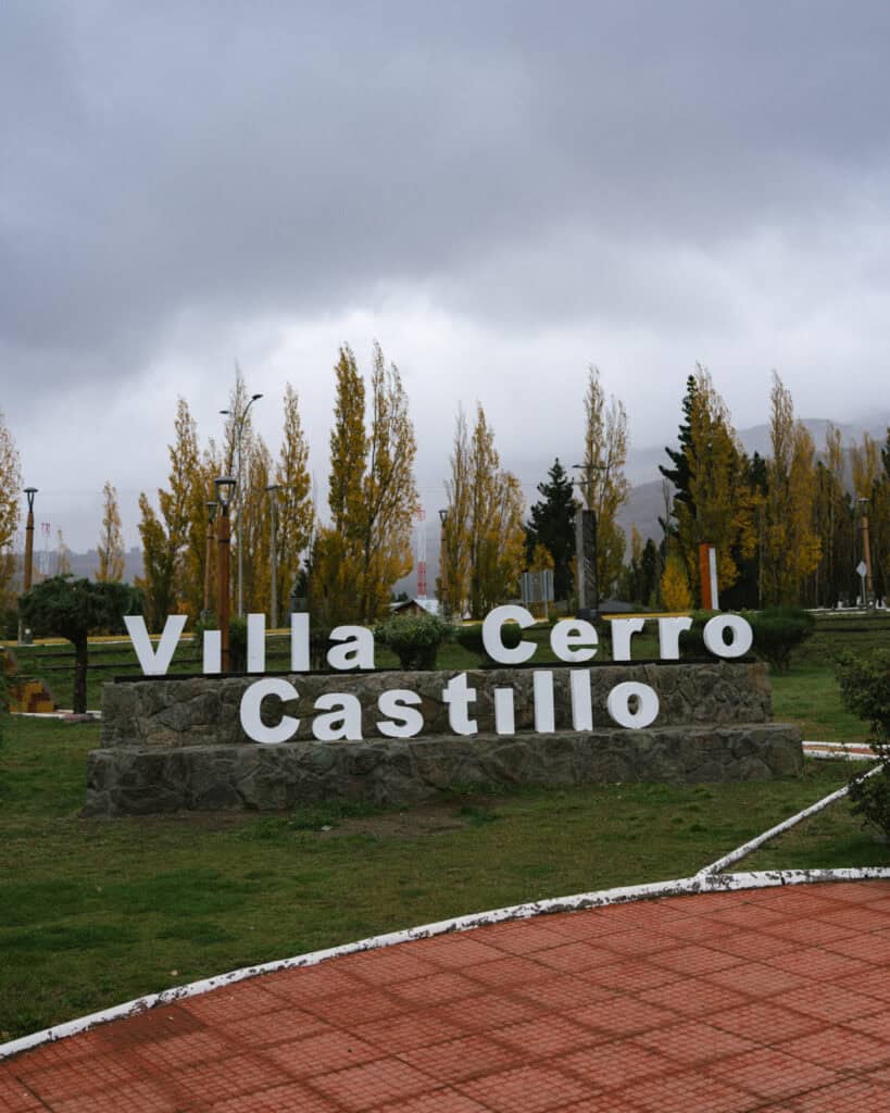 Villa Cerro Castillo, Chile Travel Guide: Hiking & Huemuls 5 A stone monument with bold white letters spelling "Villa Cerro Castillo" sits in a manicured park, surrounded by autumnal trees under an overcast sky