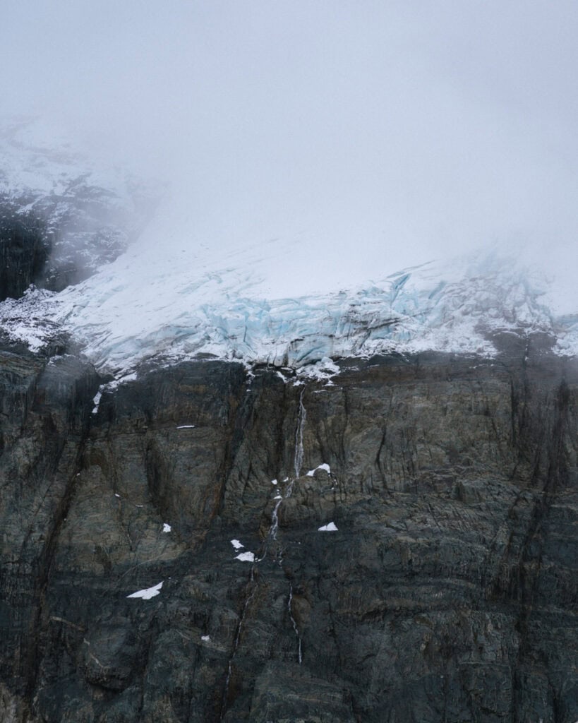 Villa Cerro Castillo, Chile Travel Guide: Hiking & Huemuls 15 Glacial ice clings to the top of a dark, sheer rock wall in Villa Cerro Castillo National Park, with melting snow feeding a narrow waterfall cascading down