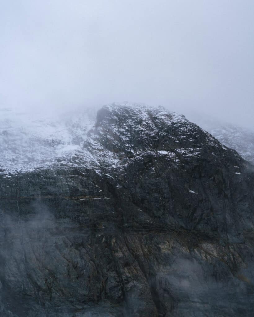 Laguna Cerro Castillo, Chile Hiking Guide 7 A close-up view of a massive rock face dusted with snow at the summit, emerging from the clouds in Villa Cerro Castillo National Park