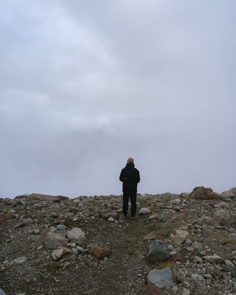 Laguna Cerro Castillo, Chile Hiking Guide 19 Brayden faces a thick fog wall while standing on a rocky mountain path in Villa Cerro Castillo, surrounded by mist and rugged terrain