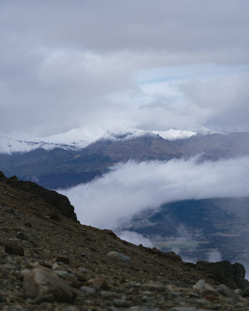 Laguna Cerro Castillo, Chile Hiking Guide 25 Snow-dusted mountains rise beyond a rocky slope with low clouds drifting between peaks in Villa Cerro Castillo National Park