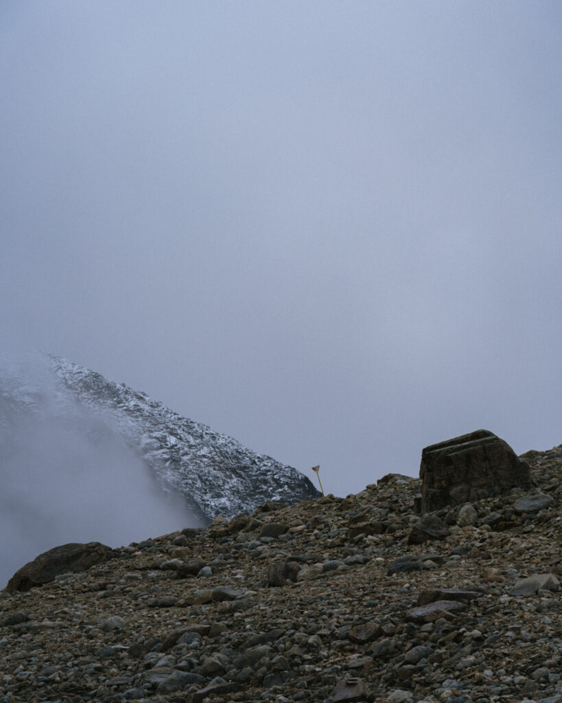 Laguna Cerro Castillo, Chile Hiking Guide 11 A lone trail marker stands among large rocks and gravel near the summit in Villa Cerro Castillo National Park, with a cloud-covered peak in the background