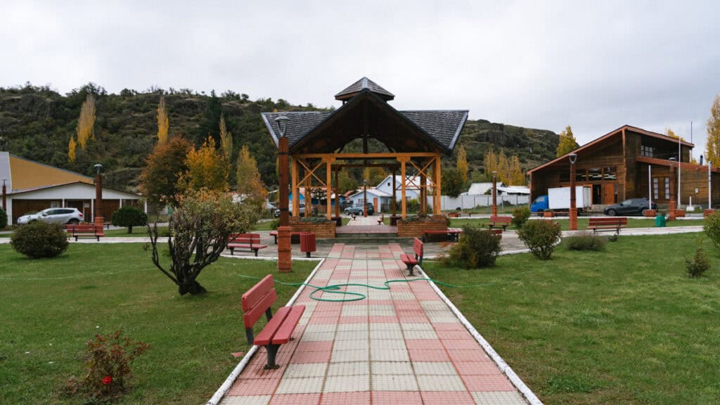Villa Cerro Castillo, Chile Travel Guide: Hiking & Huemuls 28 A symmetrical view of the Villa Cerro Castillo plaza features a covered wooden gazebo at its center, surrounded by red benches, tidy lawns, and autumn trees