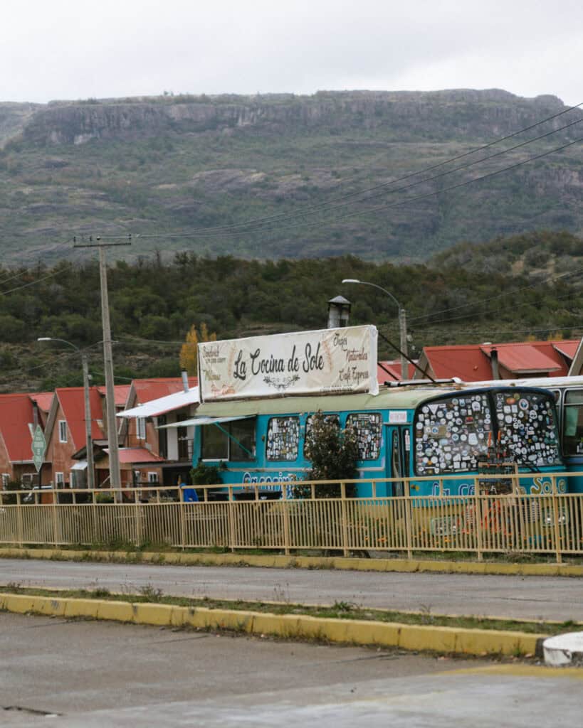 Villa Cerro Castillo, Chile Travel Guide: Hiking & Huemuls 26 A vibrant turquoise food bus named “La Cocina de Sole” is parked behind a yellow fence, with its windows plastered in stickers and a hand-painted sign advertising empanadas, natural juices, and espresso