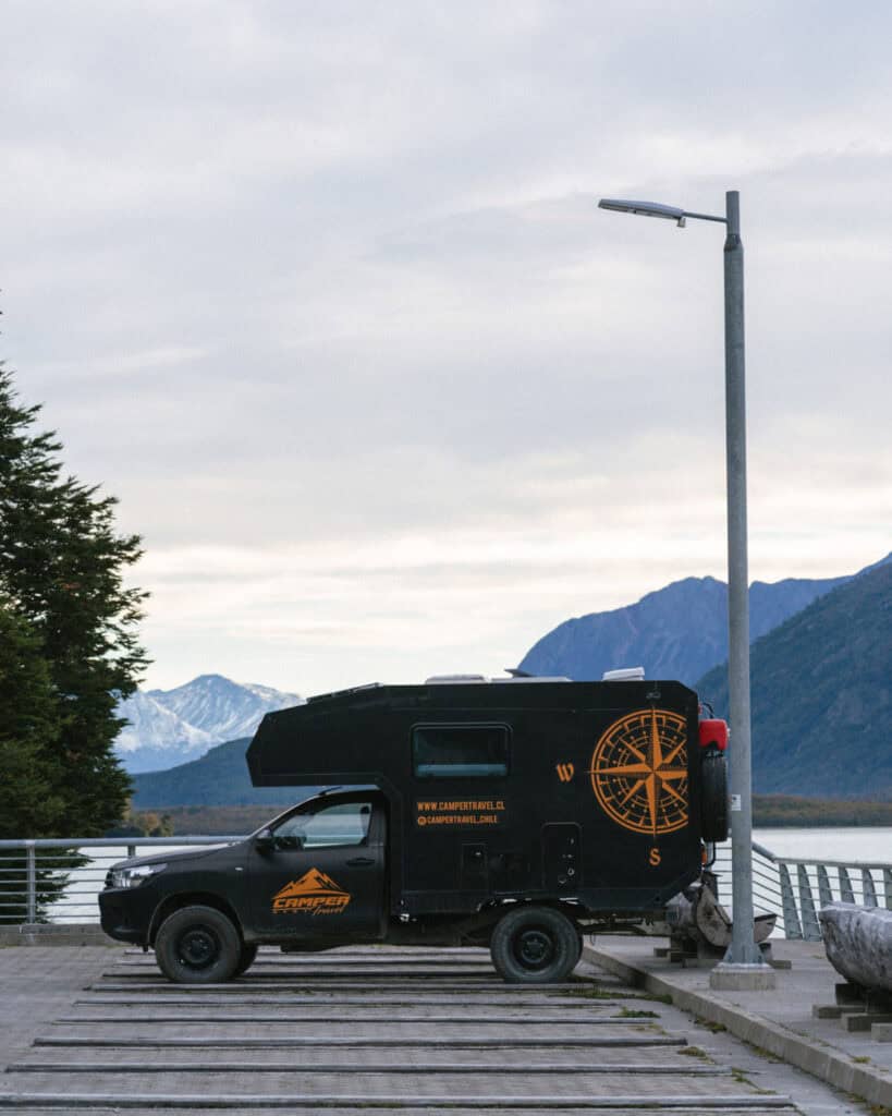 Camping on the Carretera Austral, Chile: Our Tips & Tricks 9 Side view of a black Camper Travel Chile van parked near the lakeside in Bahía Bahamondes, with a scenic backdrop of snowy mountain peaks and peaceful water