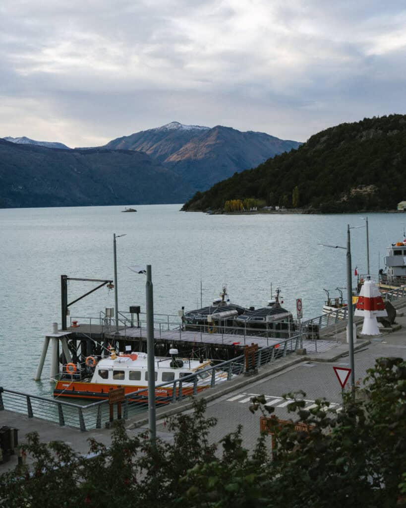 Villa O'Higgins, Chile Guide: End of the Carretera Austral 26 A small port at Bahía Bahamondes on Lago O’Higgins, featuring docked boats including one labeled “Patagonia,” with misty mountains and a dramatic cloudy sky in the distance