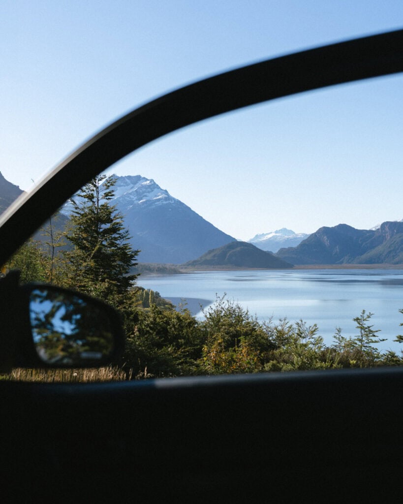 The Carretera Austral, Chile: Everything You Need to Know 52 Serene glimpse through a car window toward the blue waters of a lake and snow-dusted mountains in the Villa O'Higgins region of Chilean Patagonia