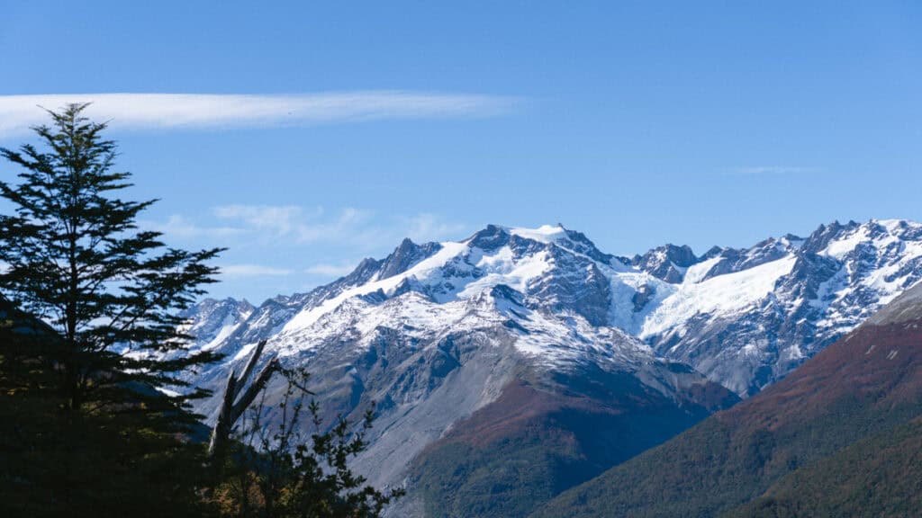 Villa O'Higgins, Chile Guide: End of the Carretera Austral 5 A sweeping view of Glaciar Mosco near Villa O'Higgins, with jagged snow-covered peaks under a bright blue sky framed by pine trees