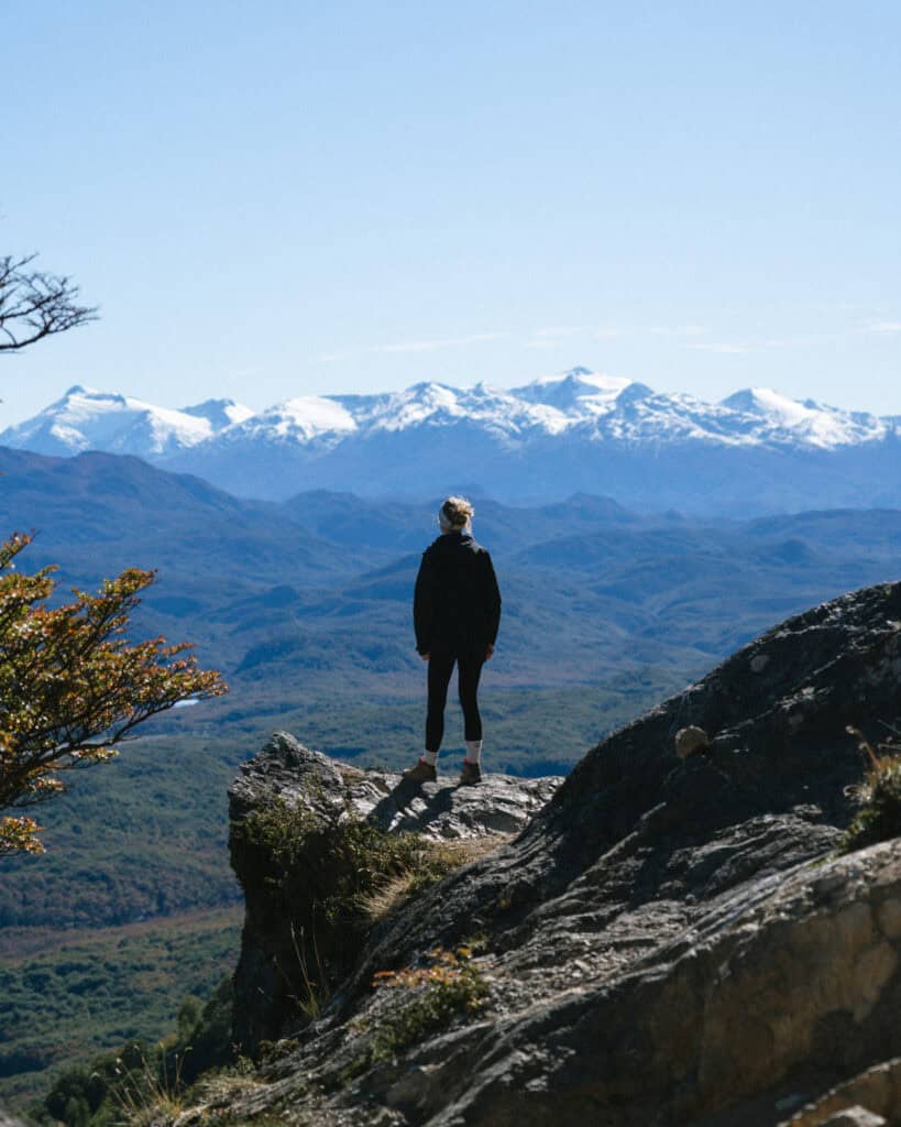 Villa O'Higgins, Chile Guide: End of the Carretera Austral 3 Sally in hiking gear stands on a rock at Mirador La Bandera, gazing toward the jagged, snow-topped Andes stretching across the horizon