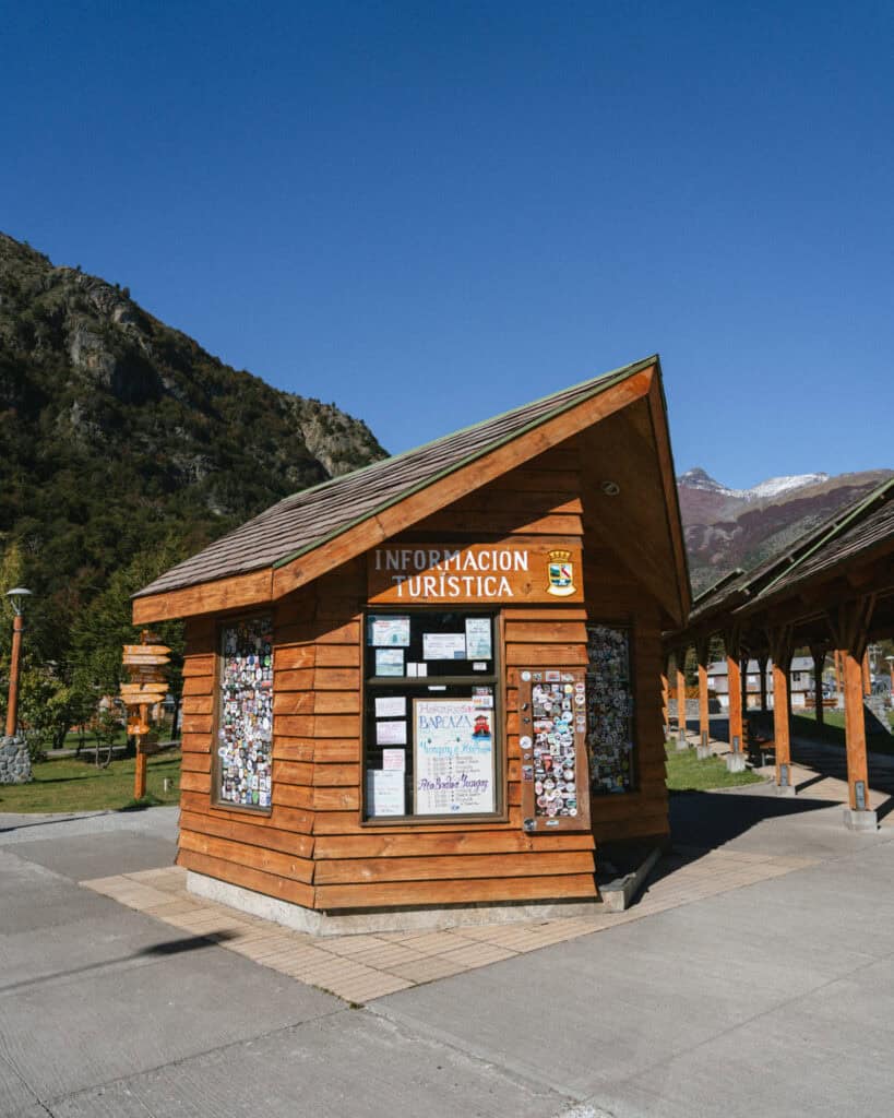 Villa O'Higgins, Chile Guide: End of the Carretera Austral 32 Wooden kiosk labeled “Información Turística” in Villa O’Higgins, decorated with travel stickers and flyers under a bright blue sky
