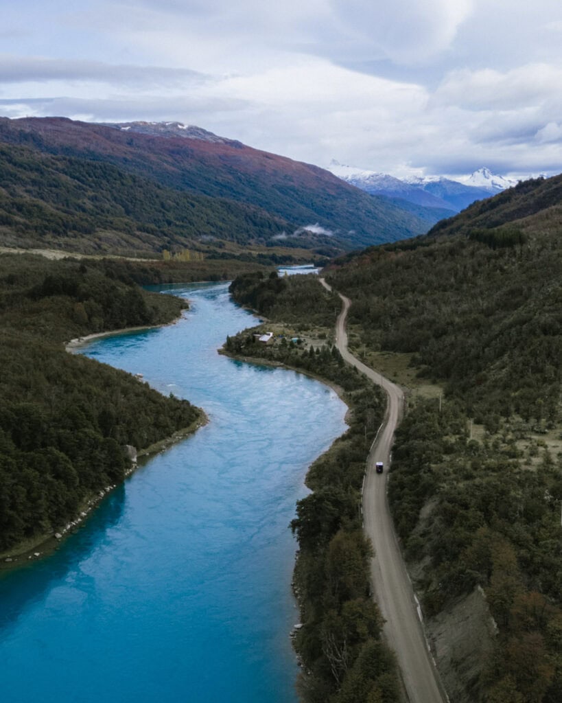 How to Visit the Marble Caves in Chile: Worth the Journey? 9 A drone shot of the bright turquoise Rio Baker on the Carretera Austral in Chile. There is a dirt road running alongside the river with a camper from Camper Travel Chile driving.