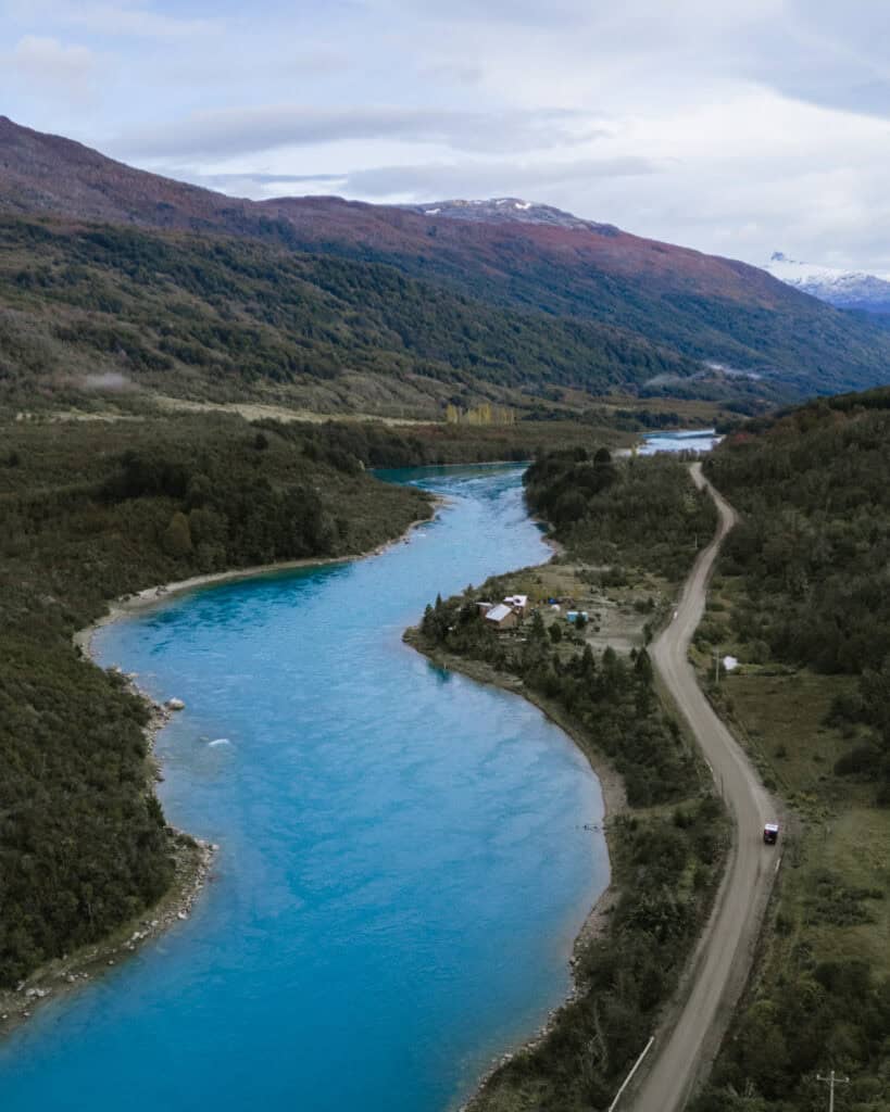 Puerto Rio Tranquilo, Chile Travel Guide: Marble & Ice 11 A drone shot of the bright turquoise Rio Baker on the Carretera Austral in Chile. There is a dirt road running alongside the river with a camper from Camper Travel Chile driving.