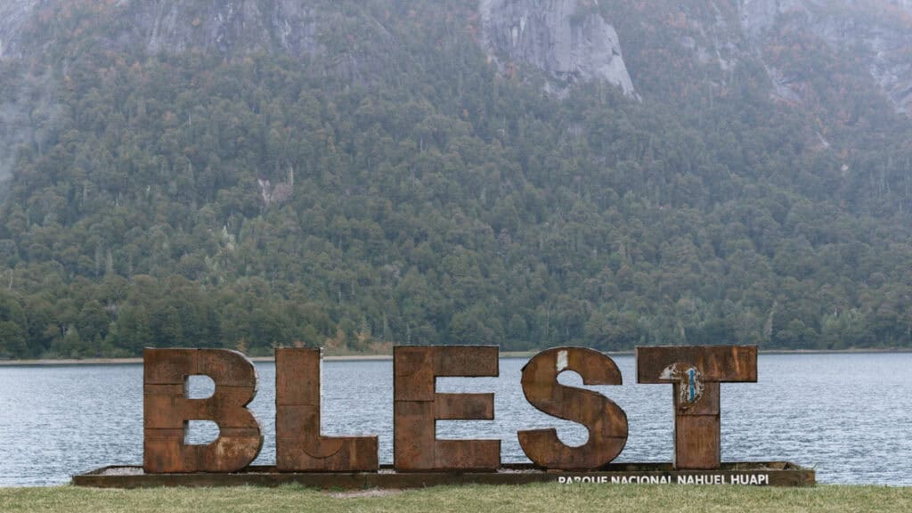 Cruce Andino: The Scenic Route From Chile to Argentina 31 Large rusty metal letters spelling “BLEST” stand on a lakeside lawn in Puerto Blest, with Parque Nacional Nahuel Huapi’s misty forested mountains in the background
