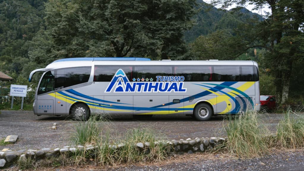 Cruce Andino: The Scenic Route From Chile to Argentina 10 A Turismo Antihual coach bus is parked beside a forest near the Petrohué dock, with a sign reading "Embarcadero Petrohué" and rugged mountains in the distance