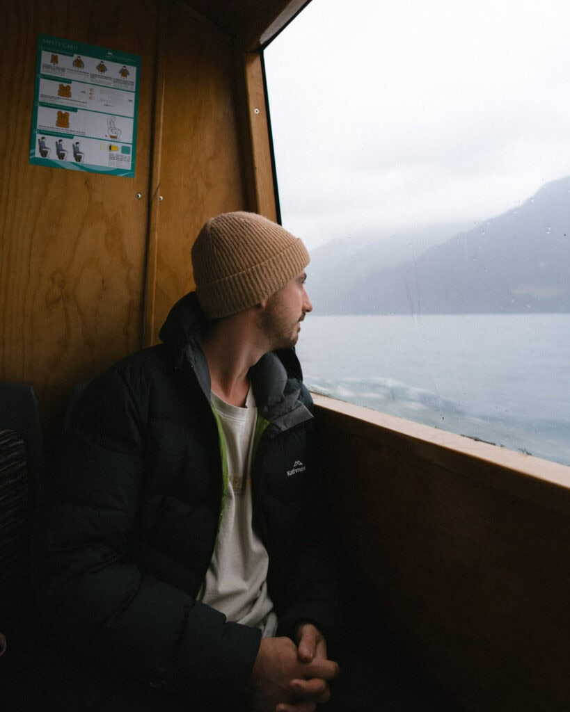 Cruce Andino: The Scenic Route From Chile to Argentina 12 Brayden, dressed in a knit cap and a black puffer jacket, gazes out a boat window at Lago Todos Los Santos, surrounded by misty Andean landscapes