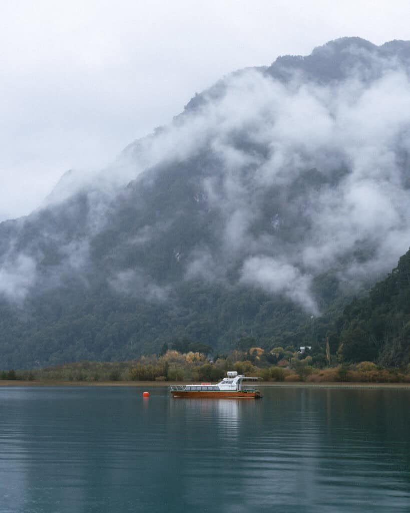 Cruce Andino: The Scenic Route From Chile to Argentina 15 A mist-covered forested mountain rises behind a solitary boat anchored on the still waters of Peulla, creating a serene, foggy Andes scene