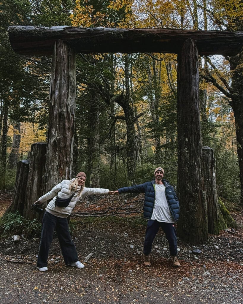 Cruce Andino: The Scenic Route From Chile to Argentina 22 Brayden and Sally hold hands under a large wooden archway surrounded by golden autumn forest foliage, marking the scenic crossing between Chile and Argentina