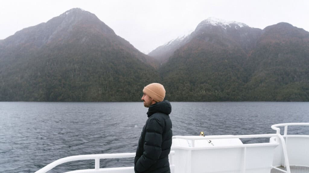 Cruce Andino: The Scenic Route From Chile to Argentina 38 Brayden stands on the deck of a boat crossing Lago Nahuel Huapi, framed by dark water and dramatic twin peaks partially dusted with snow