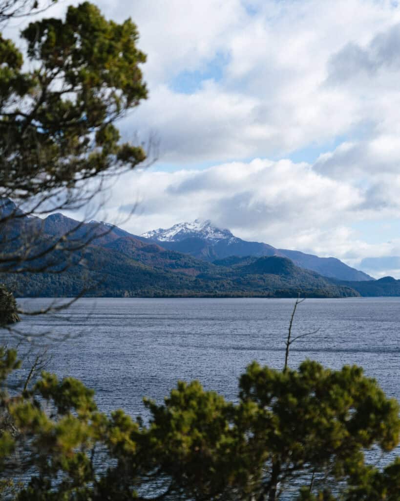 Cruce Andino: The Scenic Route From Chile to Argentina 37 View of Lago Nahuel Huapi from Puerto Pañuelo in Chile, framed by pine trees in the foreground with snow-dusted mountains and a partly cloudy sky in the distance